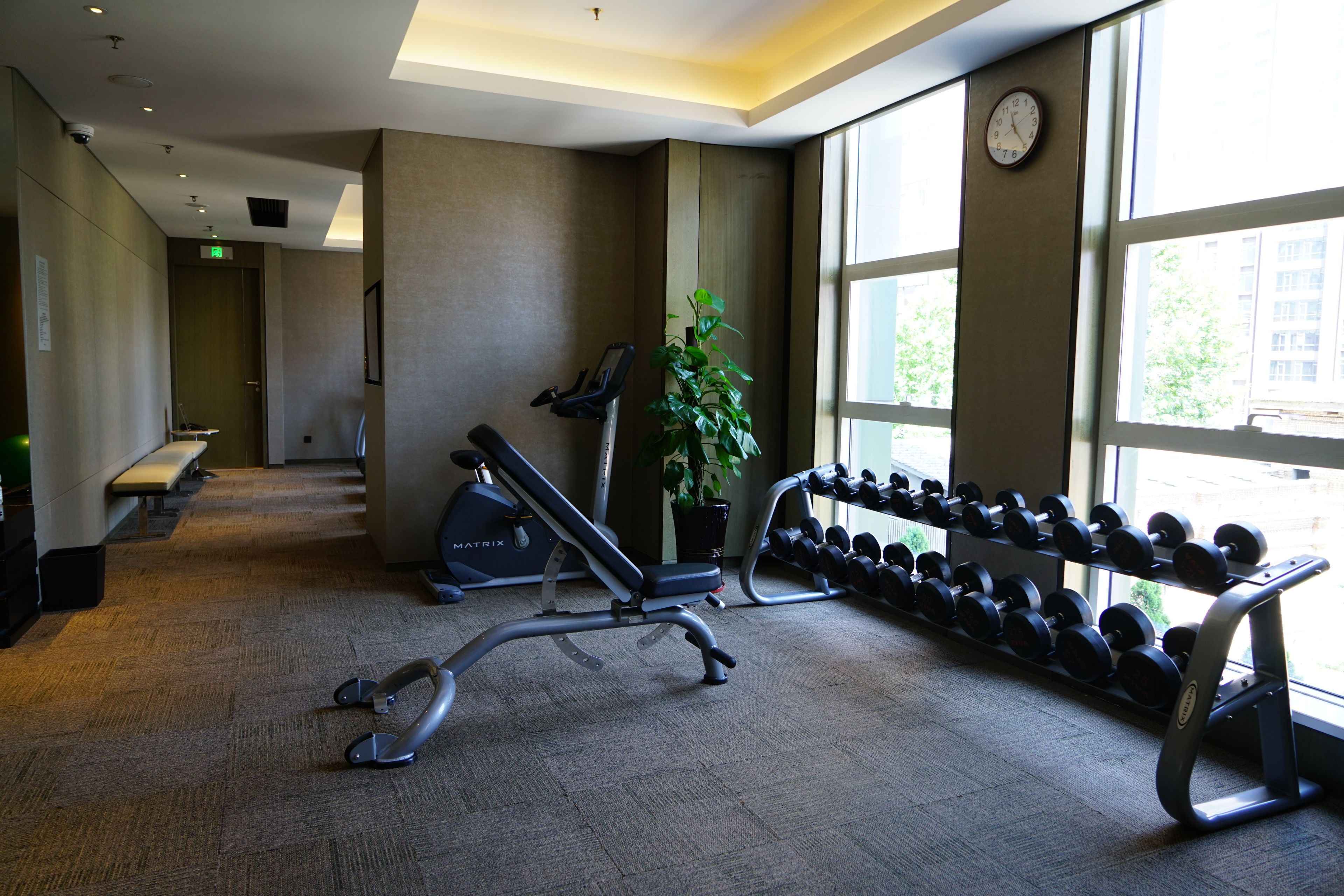 A gym with exercise equipment, a clock, and large windows.