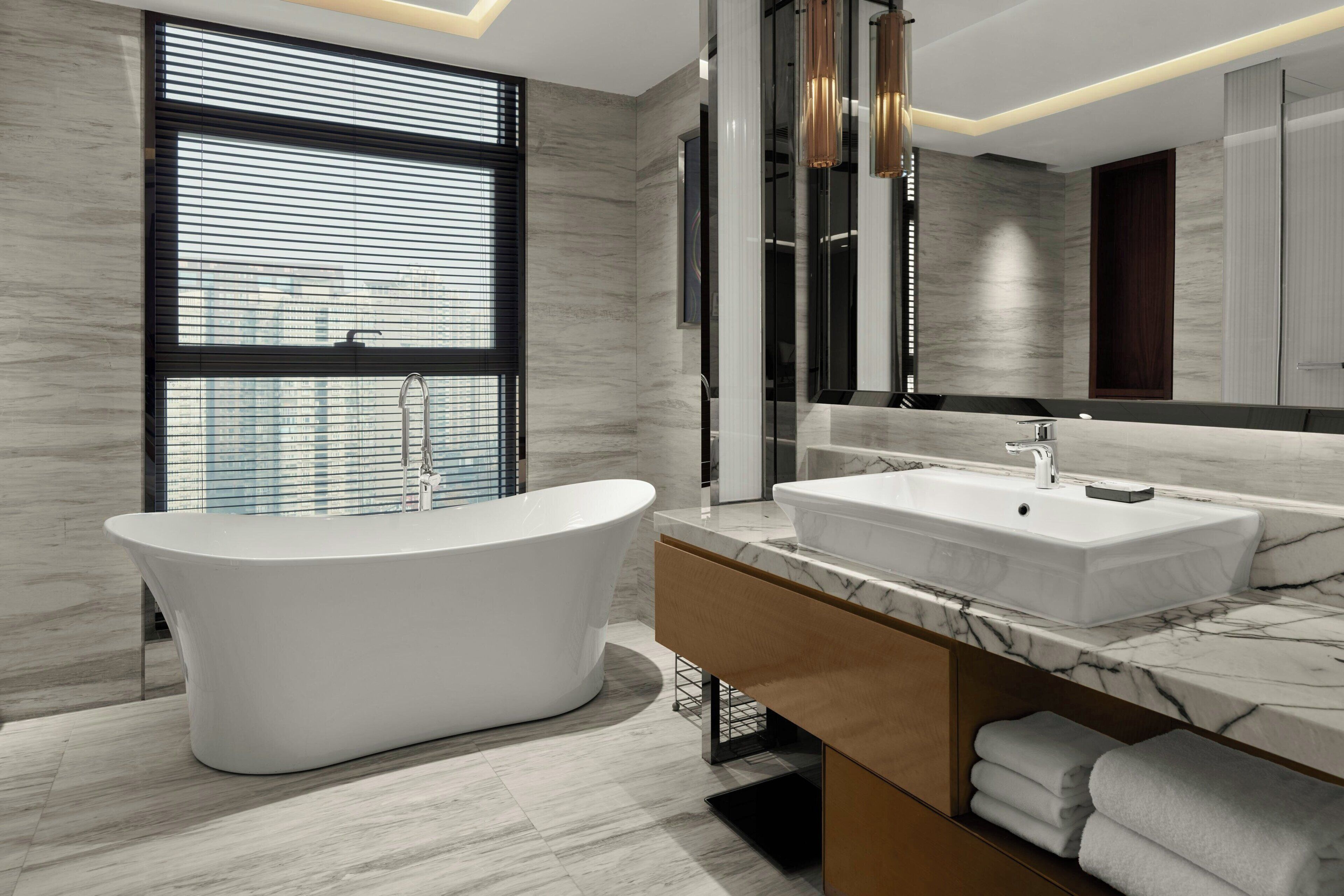 A modern bathroom with a freestanding bathtub, a large vanity with a marble countertop, and a large mirror.