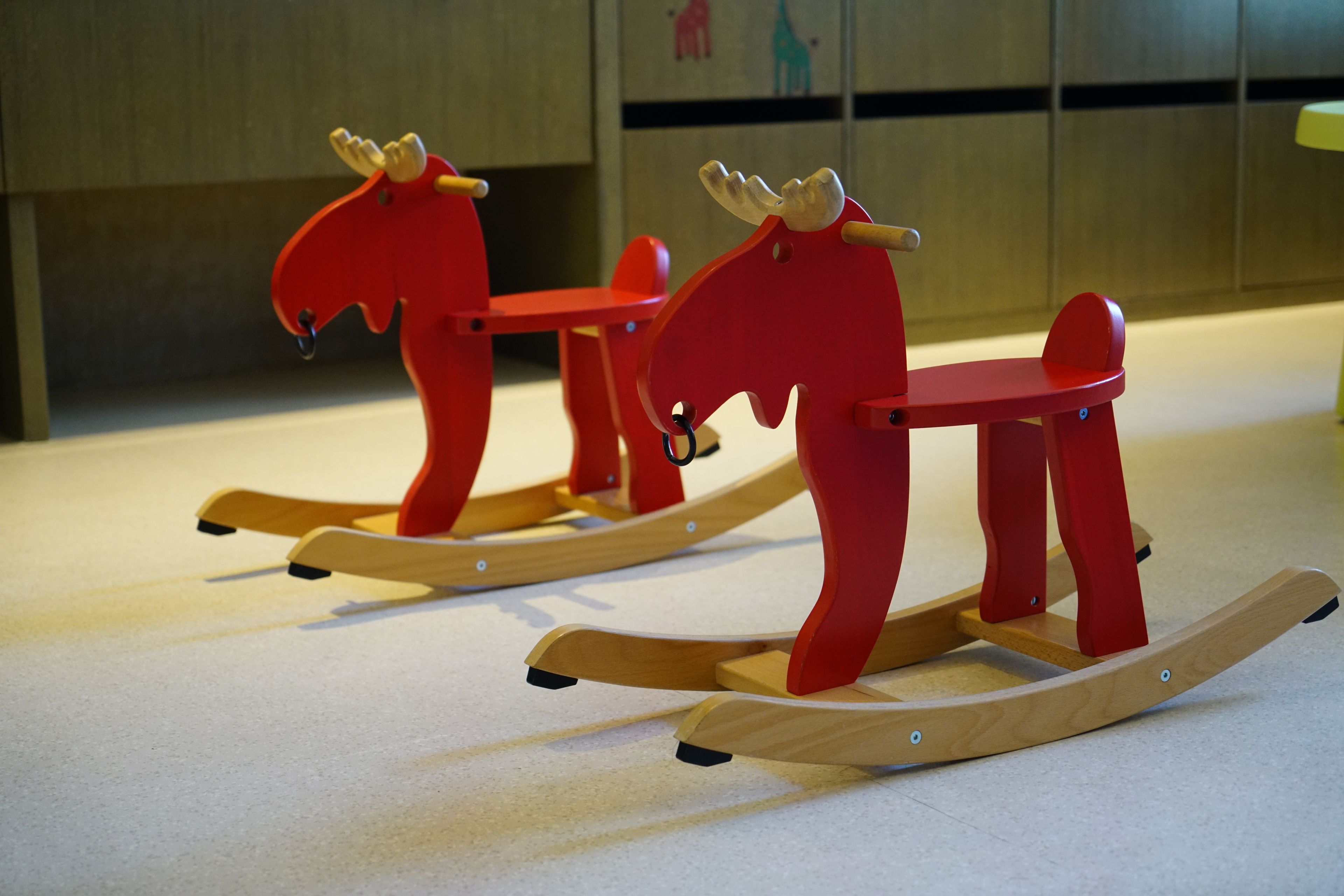 Two red rocking horses on a light-colored floor.