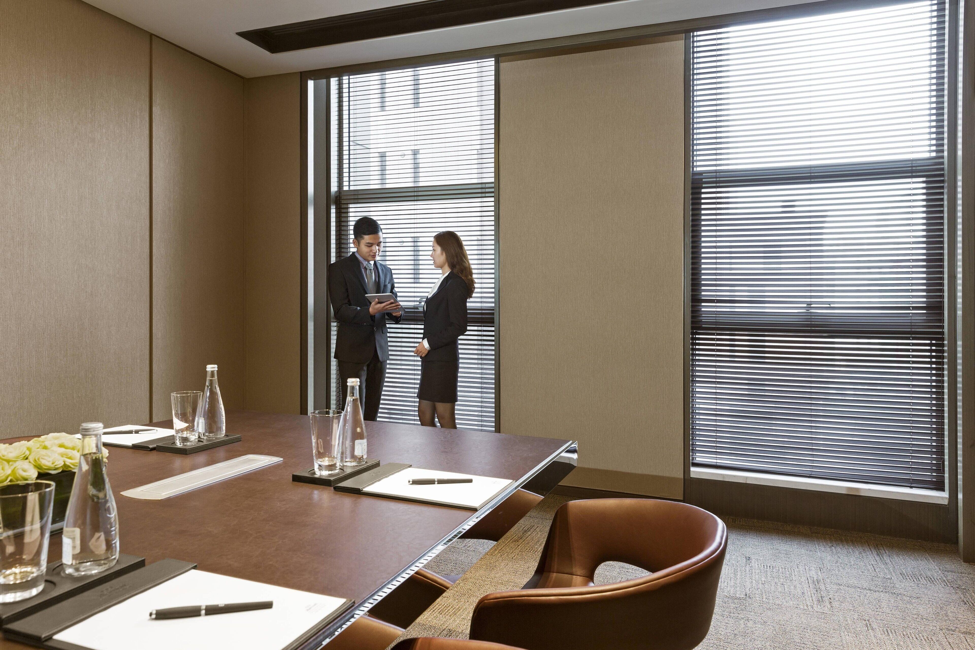 A conference room with a long table, chairs, and a window with blinds.
