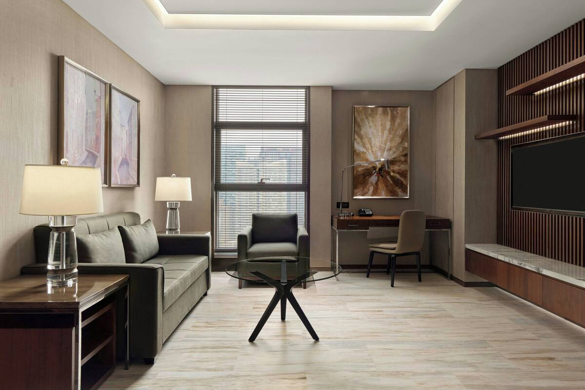 A modern hotel room with a glass coffee table, a sofa, a desk, and a TV.