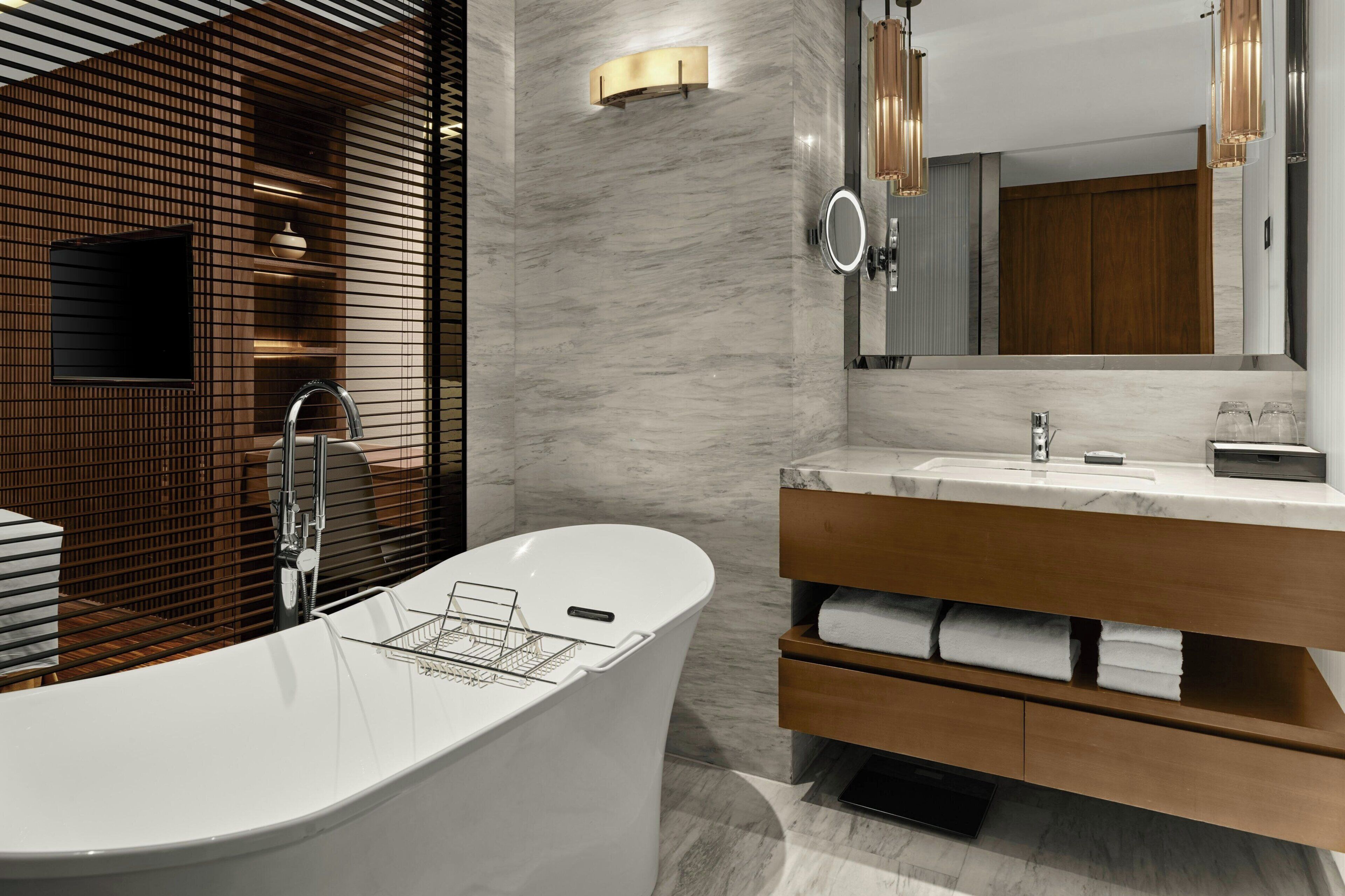 A modern bathroom with a freestanding bathtub, a vanity with a mirror, and a wooden panel wall.
