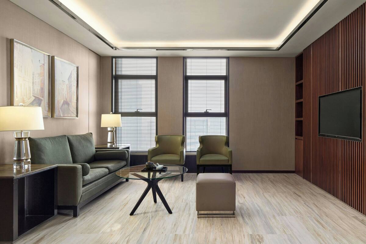A modern living room with a sofa, armchairs, a glass coffee table, and a television.