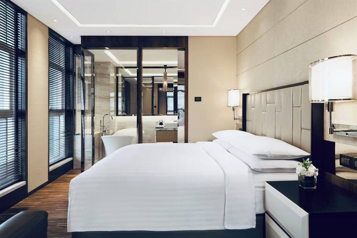 A hotel room with a large bed, a bedside table, a lamp, and a view of the bathroom.