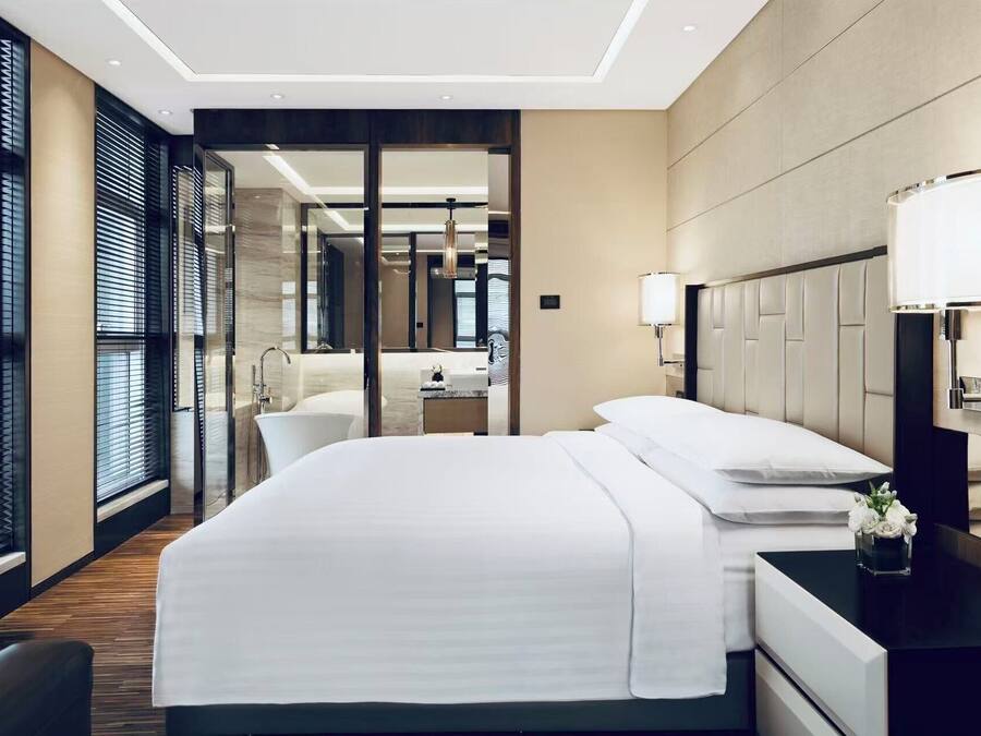 Ein Hotelzimmer mit einem großen Bett, einem Nachttisch, einer Lampe und Blick ins Bad.