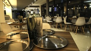 A modern restaurant interior with tables set for dining, a menu stand, and a view of the dining area. - The Nicol Hotel and Apartments (Germiston)