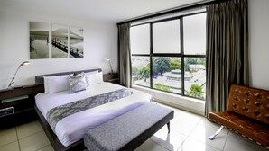 A hotel room with a large bed, a bench, a view of the city, and a painting on the wall. - The Nicol Hotel and Apartments (Germiston)