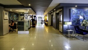 A modern hotel lobby with a reception desk, seating area, and artwork. - The Nicol Hotel and Apartments (Germiston)