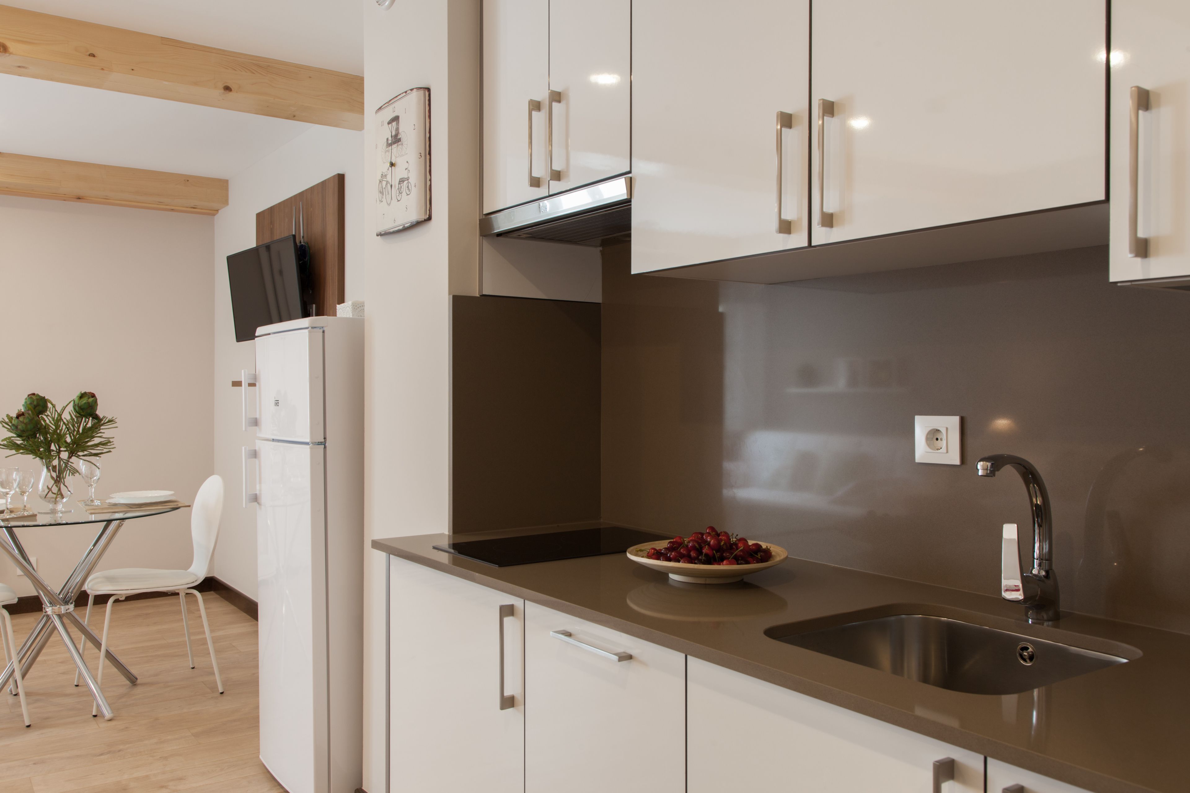 Una cucina moderna con mobili bianchi, un lavello in acciaio inossidabile e una ciotola di frutta sul bancone.