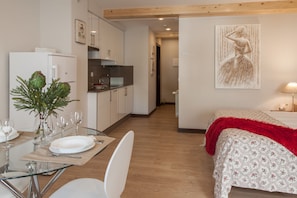 A modern kitchen with white cabinets, a stainless steel refrigerator, and a dining area with a glass table and white chairs. - Apartamentos Nova Compostela (Santiago de Compostela)