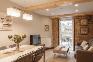 A modern living room with a dining area, stone wall, wooden beams, and a television. - Apartamentos Nova Compostela (Santiago de Compostela)