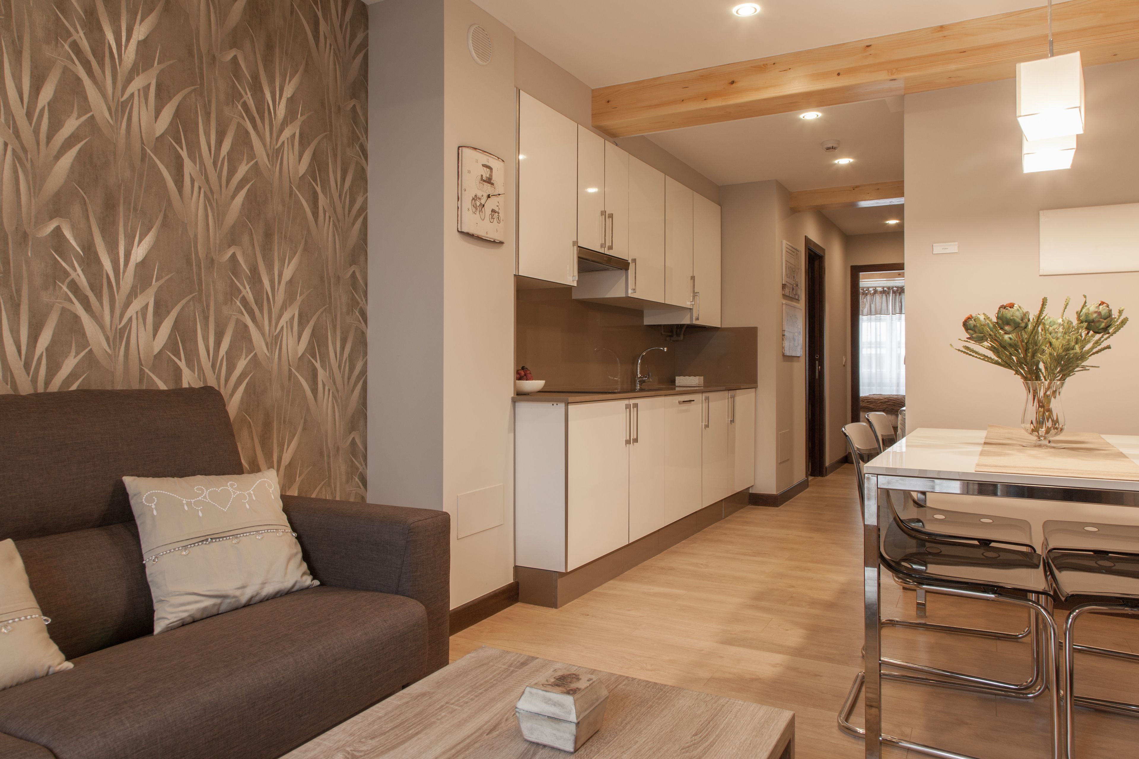 A modern living room with a sofa, a wooden coffee table, and a kitchen area with white cabinets and a dining table with bar stools.