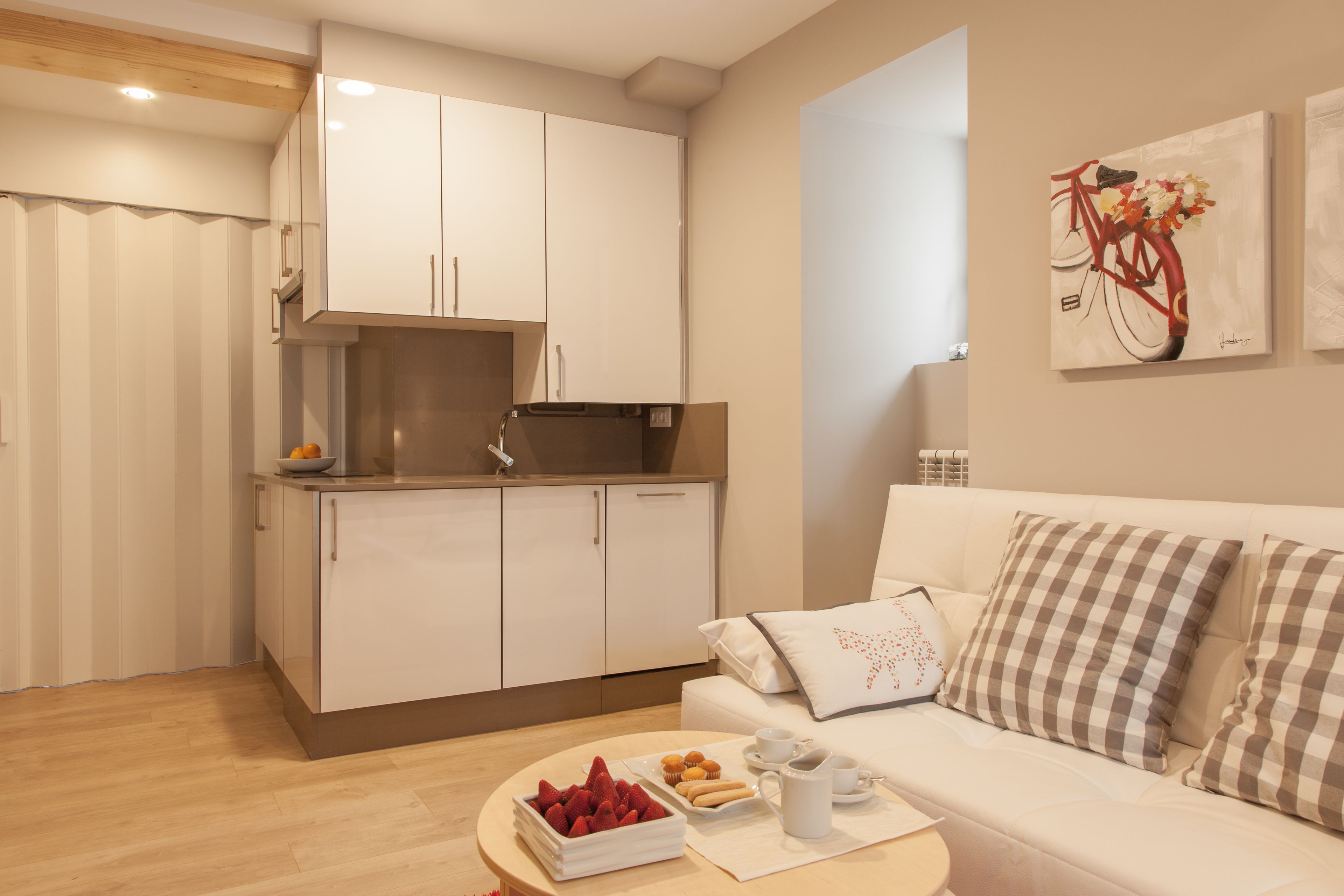 Une cuisine moderne avec des meubles blancs et un coin repas comprenant un canapé blanc et des coussins à carreaux.