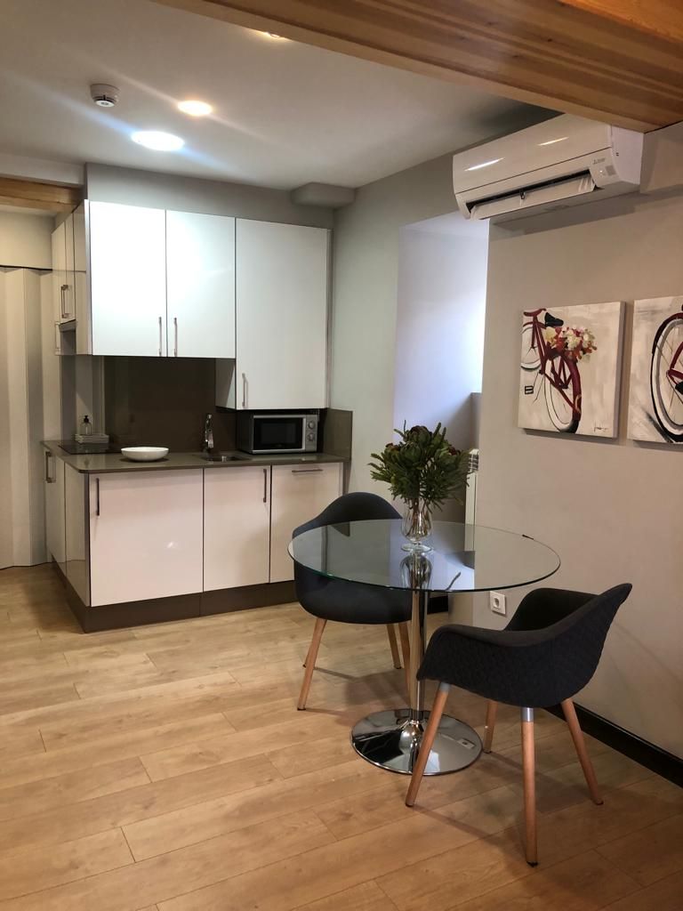 A modern kitchen with white cabinets, a microwave, and a glass dining table with two chairs.