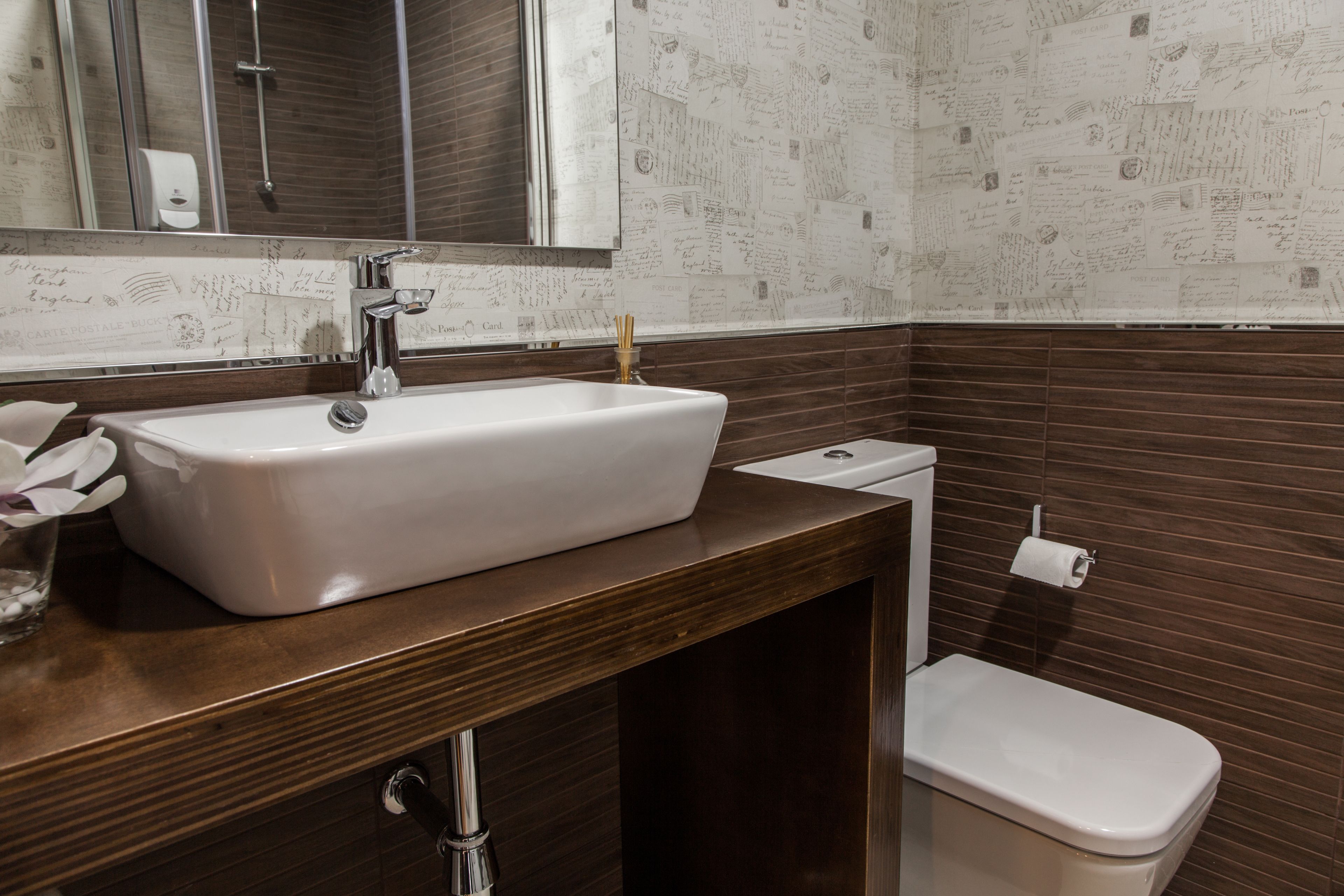 Un bany amb un lavabo blanc, un armari de tocador de fusta fosca, un mirall i un vàter.