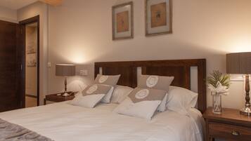 A neatly made bed with white linens and decorative pillows, a wooden headboard, a bedside table with a lamp, and framed artwork on the wall.