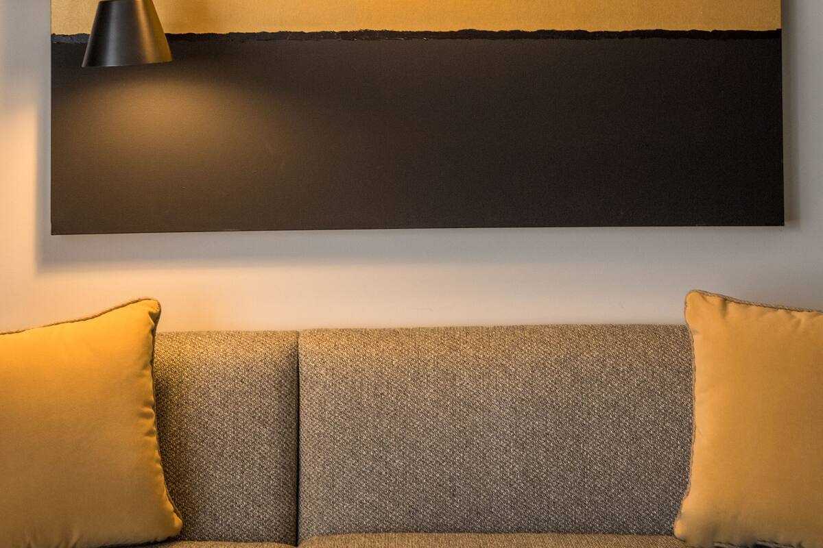 A modern room with a large wall-mounted artwork, two black floor lamps, and a grey sofa with yellow cushions.
