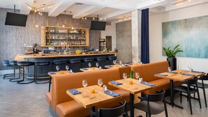 A modern bar area with a wooden counter, bar stools, and a variety of bottles. There are seating areas with tables and chairs, and a large abstract painting on the wall. - The Hi-Lo, Autograph Collection (Portland)