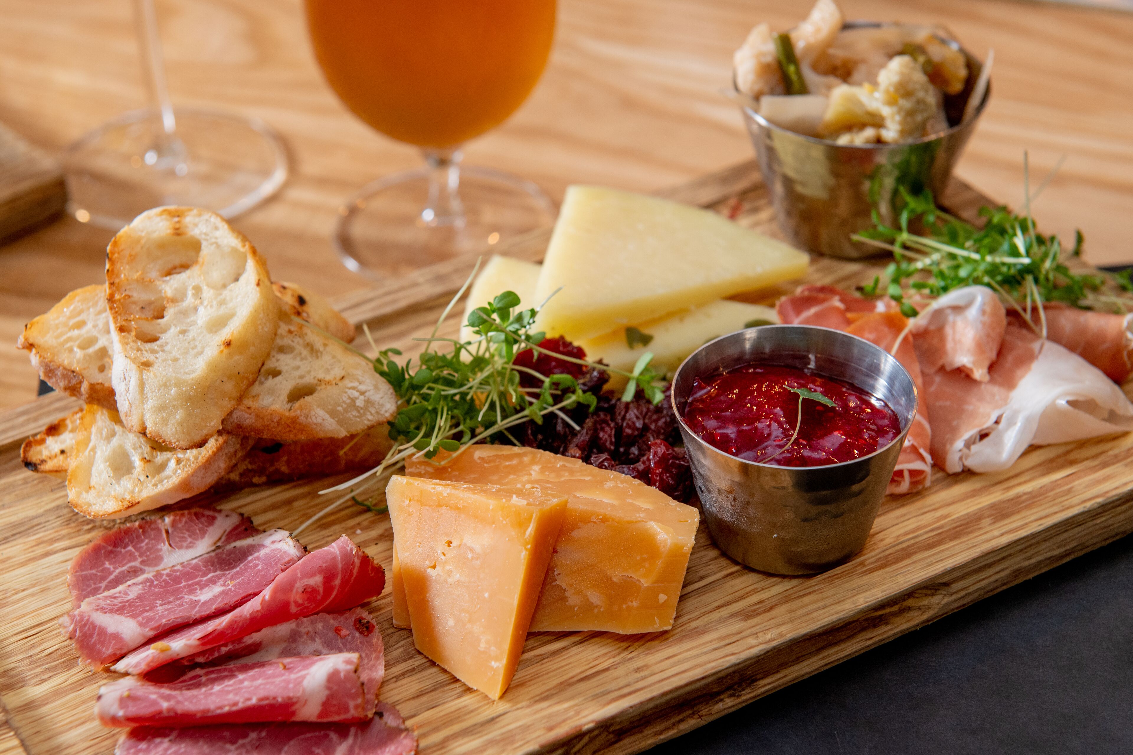 A charcuterie board with various cheeses, meats, and a glass of wine on a wooden table.