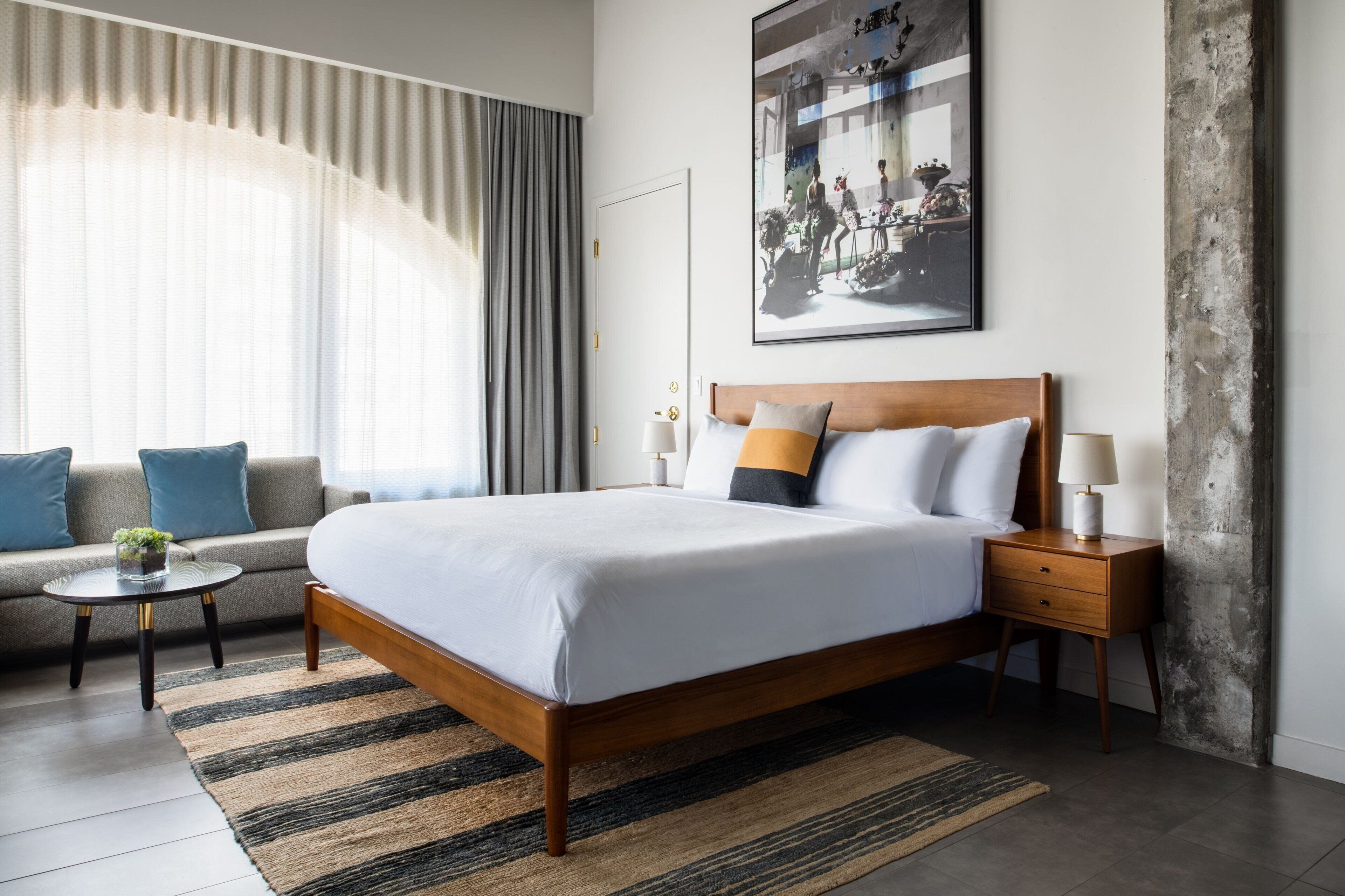 A modern hotel room with a large bed, a sofa, a small table, and a nightstand.