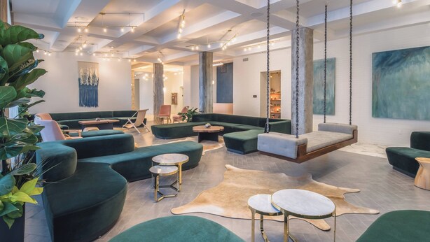 A modern lounge area with green sofas, a hanging swing, and a central coffee table. - The Hi-Lo, Autograph Collection (Portland)