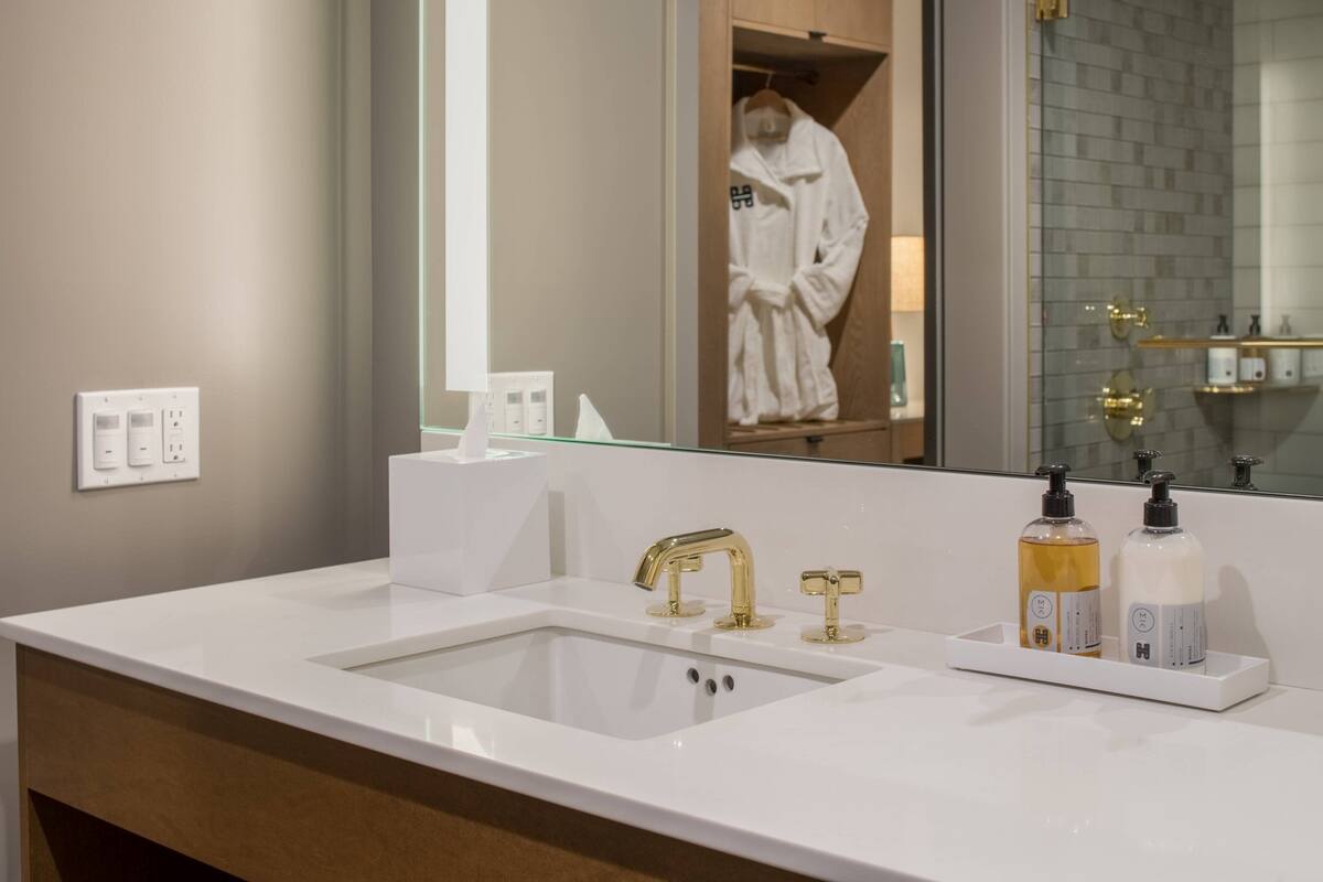 A modern bathroom with a white sink, gold faucets, and two bottles of toiletries.