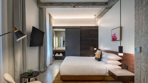 A modern hotel room with a large bed, a small desk, a chair, a TV, and a framed picture on the wall. - The Hi-Lo, Autograph Collection (Portland)