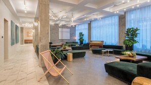 A modern lobby with a marble floor, green sofas, a wooden bench, and potted plants. - The Hi-Lo, Autograph Collection (Portland)