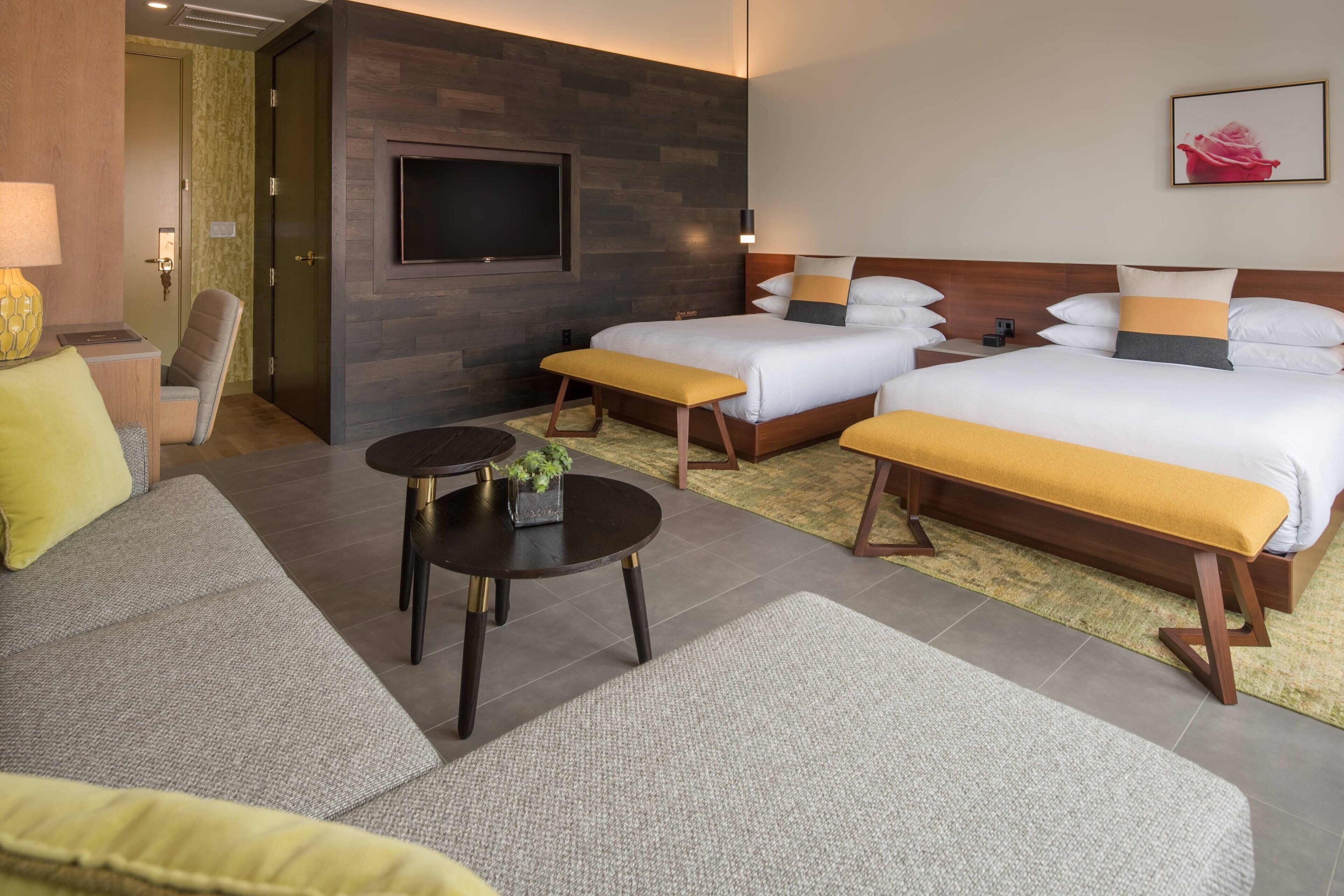 A hotel room with two beds, a sofa, a small table, and a TV mounted on the wall.