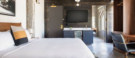 Une chambre d’hôtel moderne dotée d’un grand lit, d’un bureau, d’une chaise, d’un téléviseur à écran plat et d’une salle de bain visible à travers une porte ouverte.