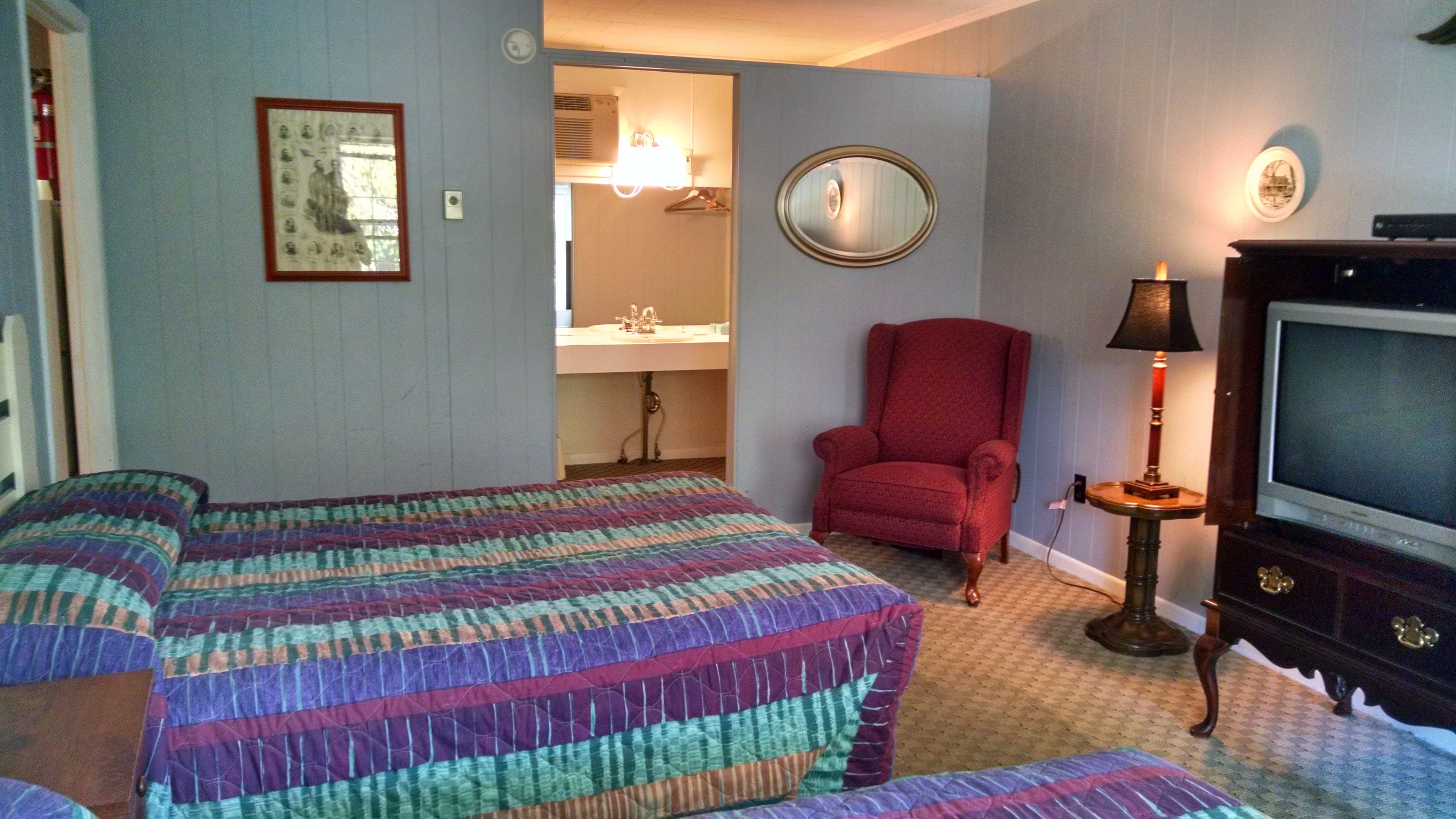 A hotel room with two beds, a red armchair, a television, and a mirror on the wall.
