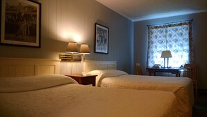 A hotel room with two beds, a nightstand with a lamp, a framed picture on the wall, a window with curtains, and a chair.