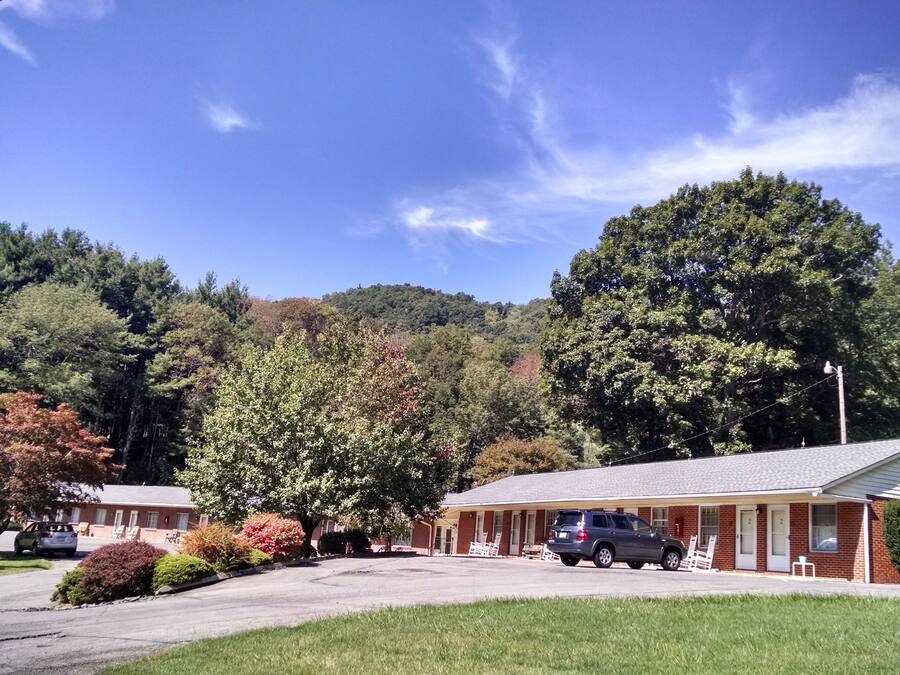 A two-story motel with a parking area, surrounded by trees and a hilly landscape.