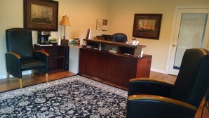 A reception area with a wooden desk, two black chairs, a patterned rug, and framed pictures on the walls.