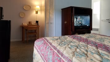 A hotel room with a bed, a wooden nightstand with a lamp, a television, and a closet with a sliding door.