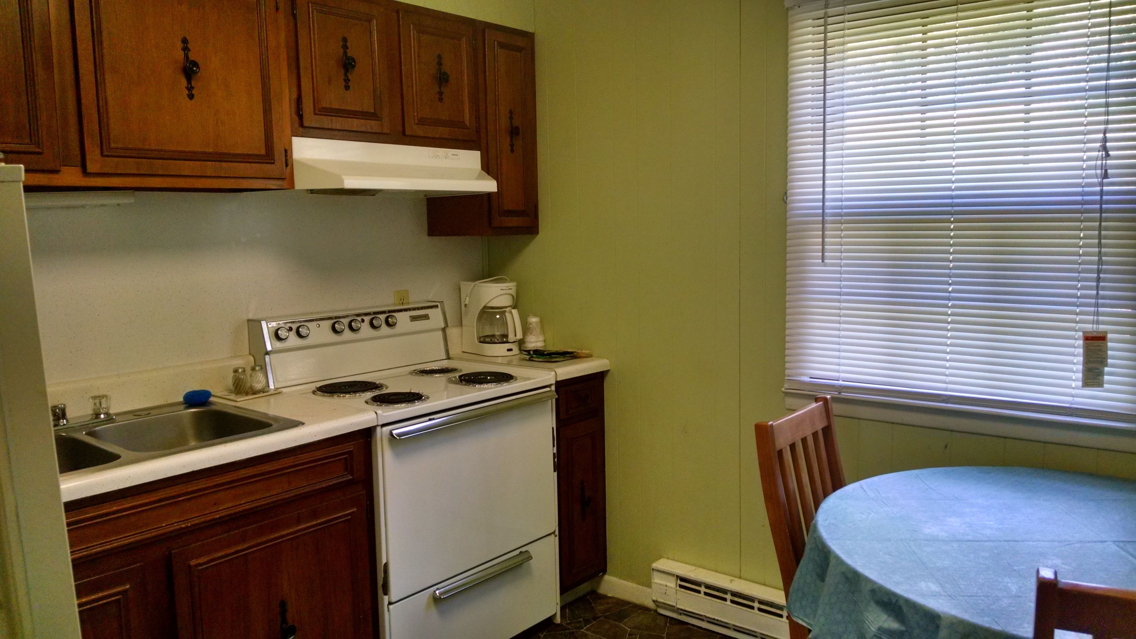 A kitchen with wooden cabinets, a stove, a coffee maker, and a window with blinds.