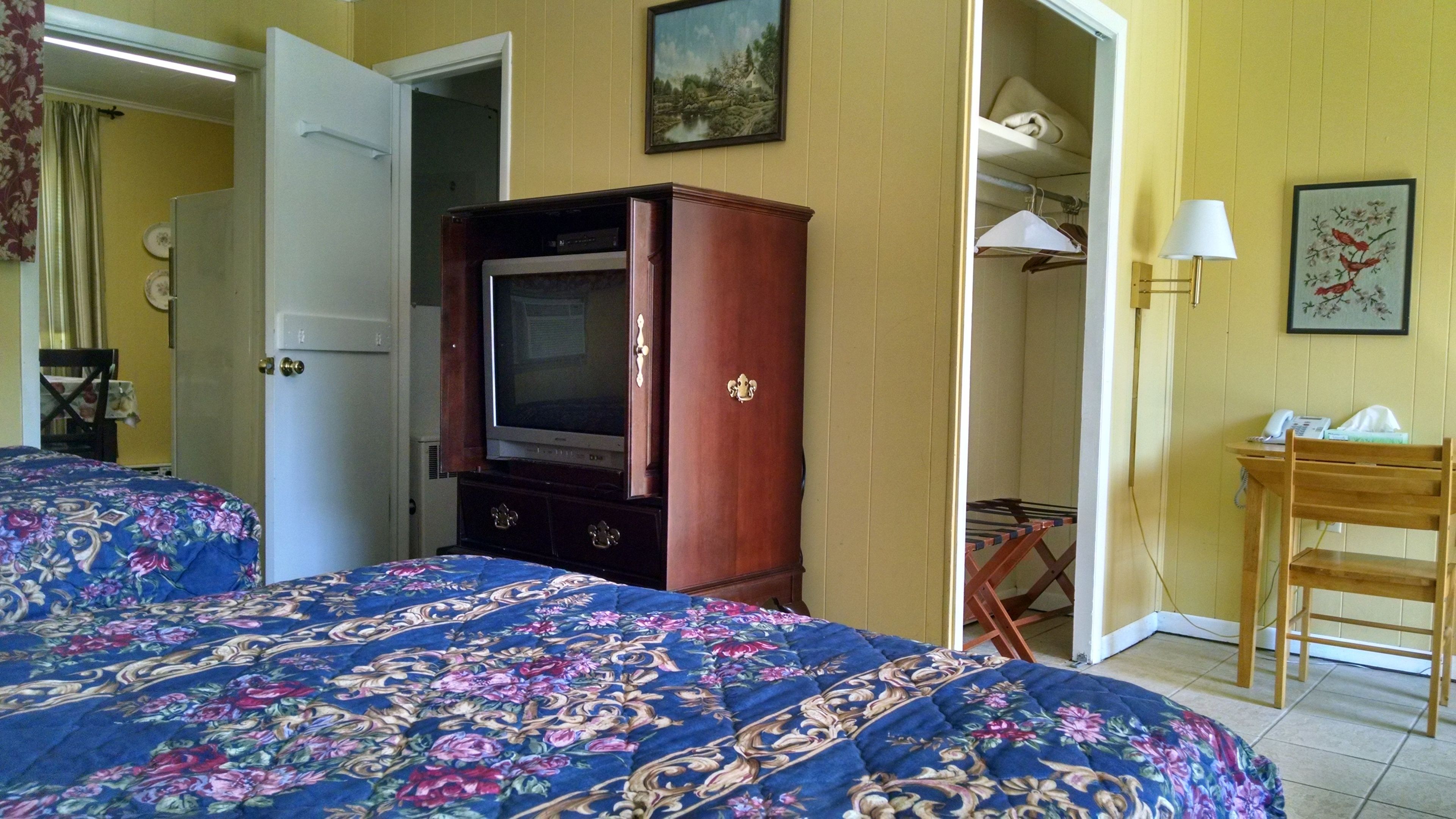 A hotel room with a bed, a television, a wardrobe, and a desk with a lamp.