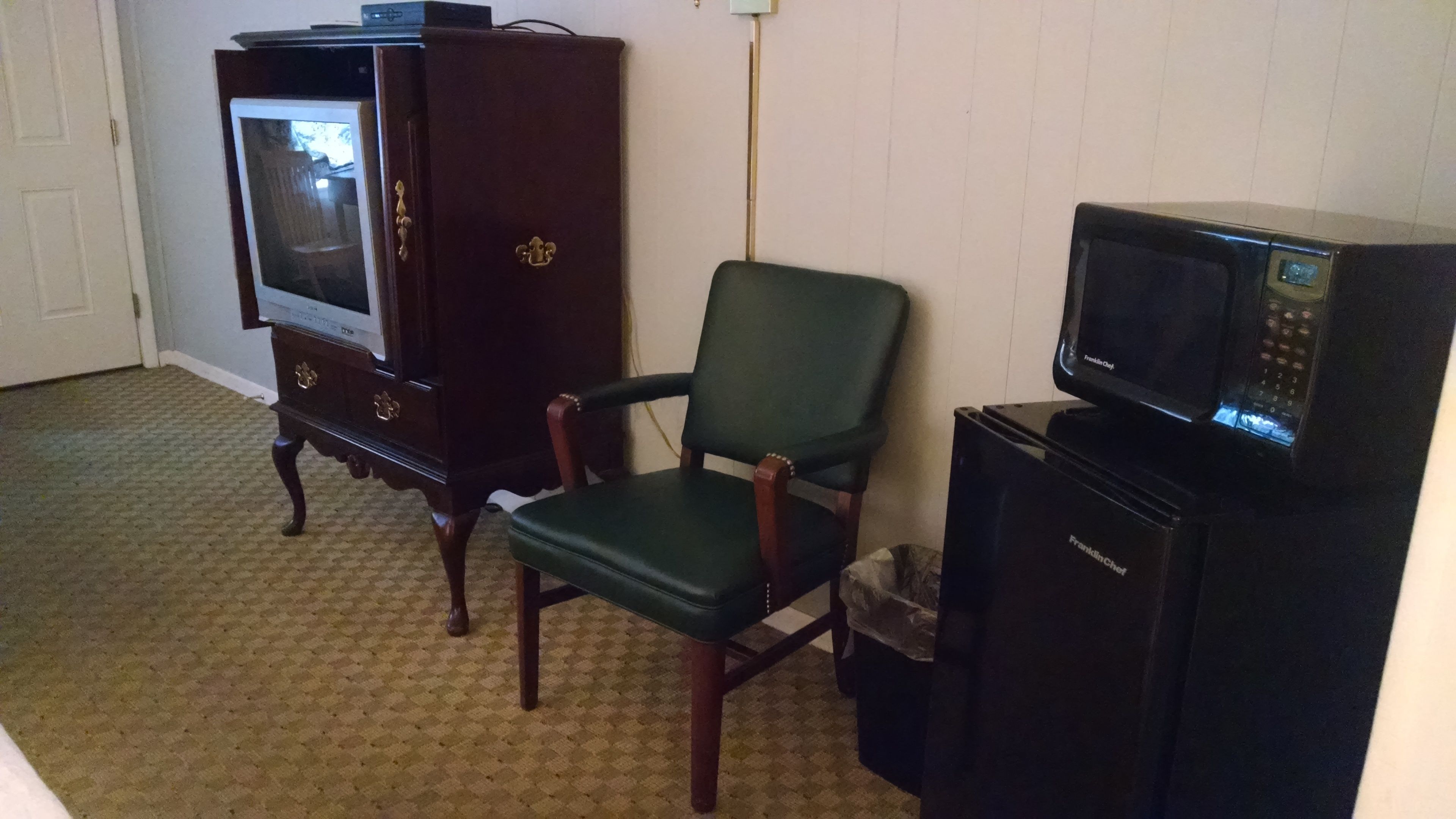 Una habitación con un televisor antiguo, un sillón verde y un refrigerador negro.