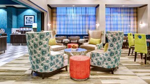 A hotel lobby with a checkered floor, patterned armchairs, a round red ottoman, and a bar area in the background. - Hampton Inn & Suites by Hilton Atlanta Perimeter Dunwoody (Atlanta)