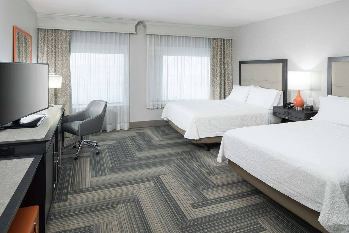 Une chambre d’hôtel avec deux lits, un bureau, une chaise, une télévision et une lampe.