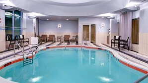 A large indoor swimming pool with a tiled edge, surrounded by seating areas and a door leading to another room. - Hampton Inn & Suites by Hilton Atlanta Perimeter Dunwoody (Atlanta)