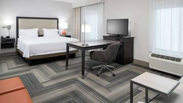 A hotel room with a large bed, a desk, a chair, a TV, and a heater.
