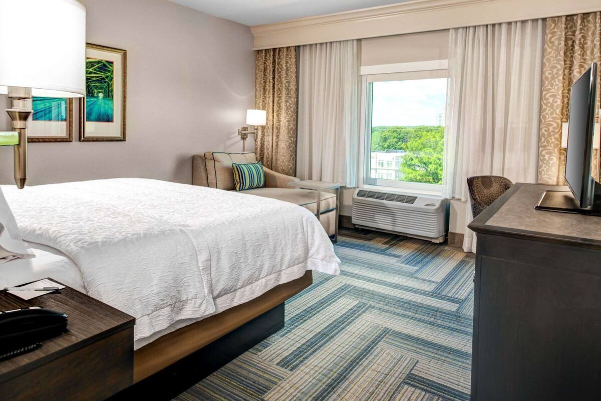 Une chambre d’hôtel équipée d’un lit, d’un bureau, d’une chaise, d’une télévision, d’une fenêtre avec des rideaux et d’un appareil de climatisation.