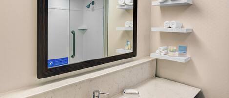 Un baño con un espejo grande, un lavamanos y repisas con toallas.
