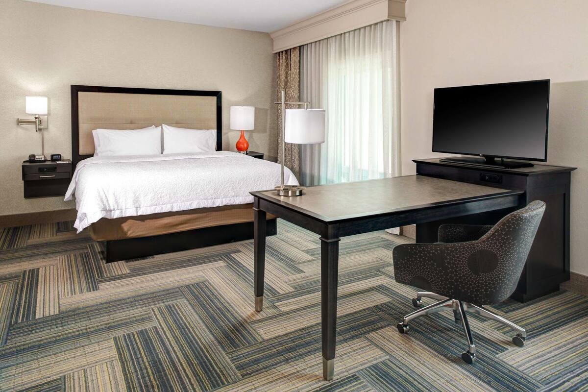 Une chambre d’hôtel équipée d’un lit, d’un bureau, d’une chaise, d’une télévision et d’une table de chevet avec une lampe.