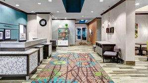 A hotel lobby with a reception desk, a clock, a bookshelf, and a patterned carpet. - Hampton Inn & Suites by Hilton Atlanta Perimeter Dunwoody (Atlanta)