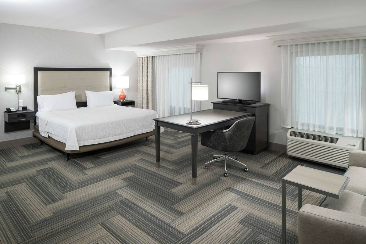 Ein Hotelzimmer mit Bett, Schreibtisch, Stuhl, Fernseher und Klimaanlage.