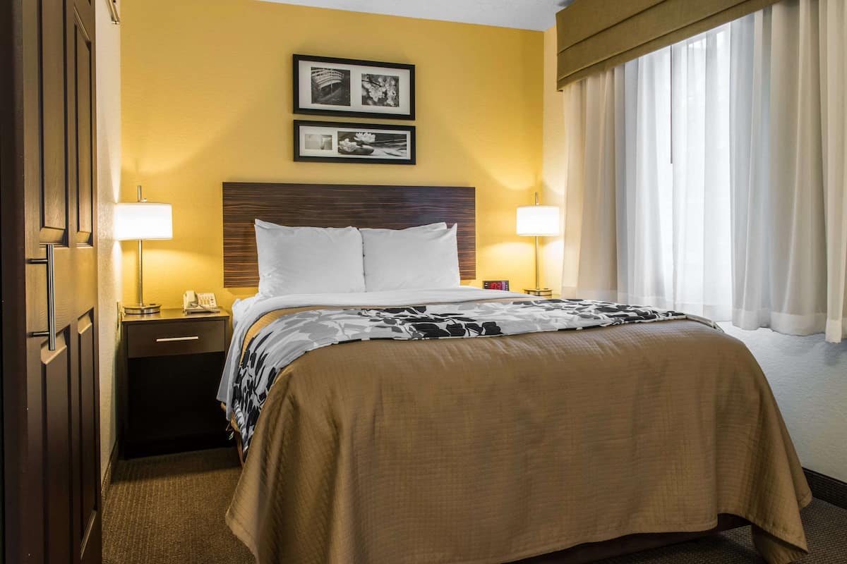A hotel room with a bed, two bedside lamps, a nightstand, a phone, and two framed pictures on the wall.