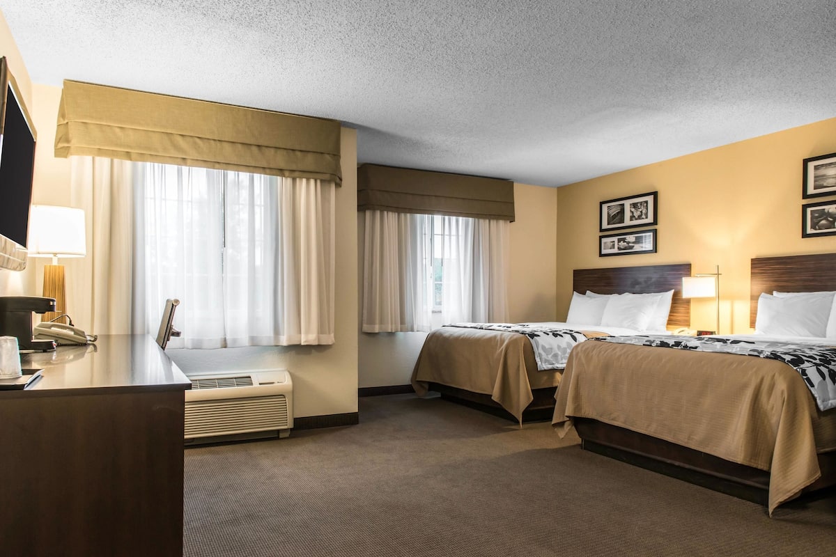 A hotel room with two beds, a desk with a telephone, and a window with curtains.