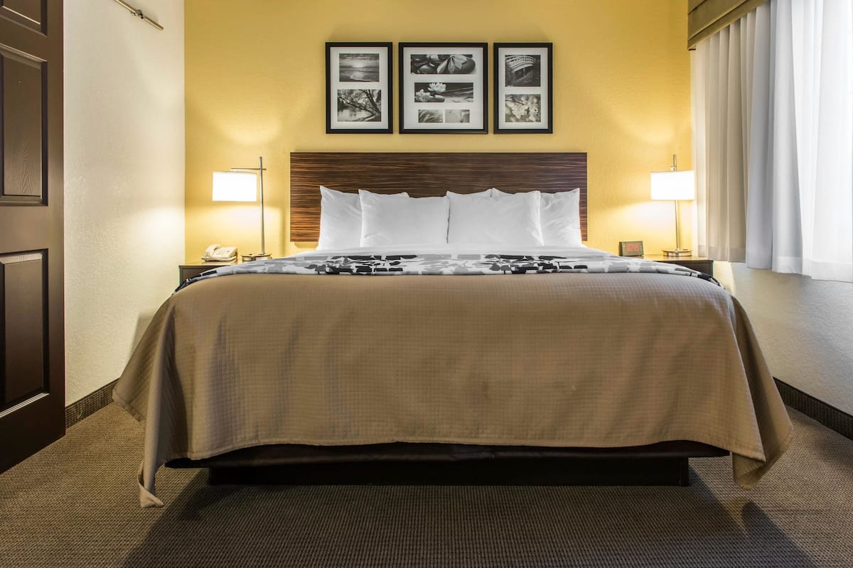 A hotel room with a large bed, a headboard, two bedside lamps, and three framed pictures on the wall.